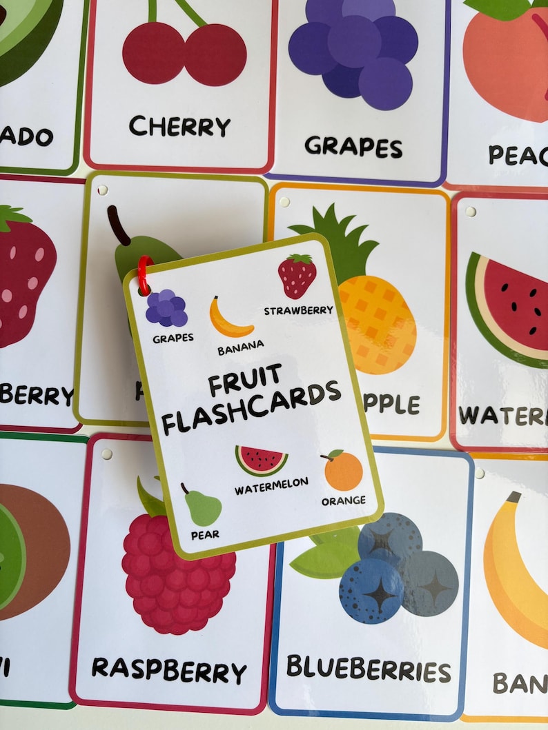 Pode incluir: Um conjunto de cart&otilde;es de mem&oacute;ria de frutas coloridas com ilustra&ccedil;&otilde;es e etiquetas. O cart&atilde;o central diz "FRUIT FLASHCARDS" e exibe imagens de melancia, laranja e pera. Outros cart&otilde;es mostram cerejas, uvas, morangos e mirtilos.