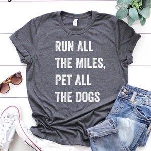 May include: Gray t-shirt with the text "Run all the miles, pet all the dogs" printed in white.