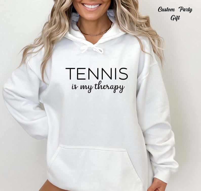 A woman wearing a white hoodie with the text "TENNIS is my therapy" printed on it.