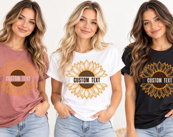 May include: Three short-sleeved crew neck t-shirts in mauve, white, and black. Each shirt features a large yellow and brown sunflower graphic on the chest with a horizontal banner across the center containing the text CUSTOM TEXT.