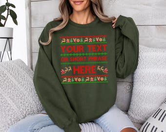 May include: An olive green crewneck sweatshirt featuring a festive holiday-themed graphic print. The design includes red and green patterns of reindeer, Christmas trees, and Santa in a sleigh, with the red text YOUR TEXT OR SHORT PHRASE HERE.
