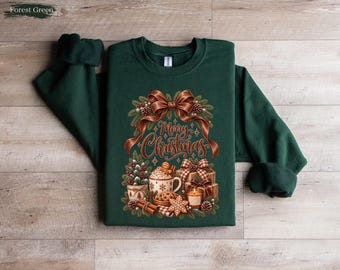 May include: A forest green long-sleeve sweatshirt featuring a graphic print of a brown ribbon, pine branches, and the text Merry Christmas. Below the text are illustrations of a mug with a gingerbread man, gift boxes, a candle, and cookies.