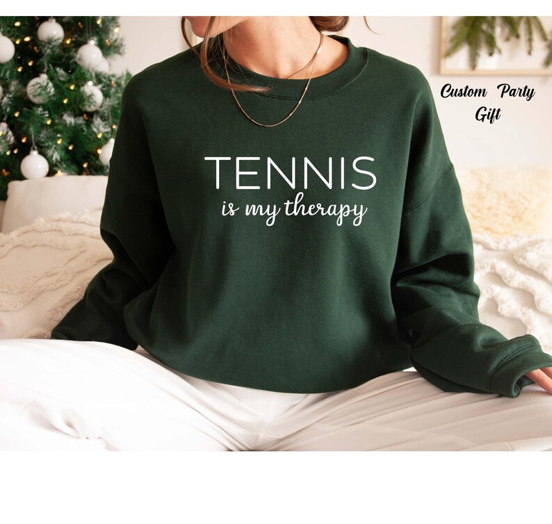 A person wearing a green sweatshirt with the text "TENNIS is my therapy" printed on it.