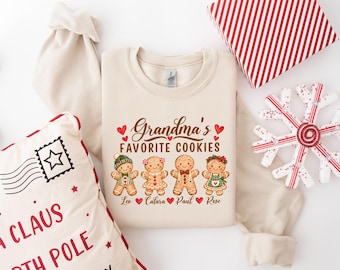 May include: A beige crewneck sweatshirt featuring a graphic of four gingerbread cookies with the text "Grandma's FAVORITE COOKIES" above them and the names "Leo", "Calara", "Paul", and "Rose" printed below each corresponding cookie.