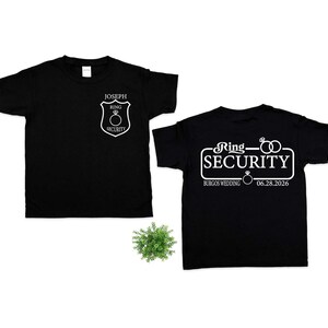 May include: Two black t-shirts with white text and graphics. One shirt features a shield design with the text "JOSEPH RING SECURITY". The other shirt has the text "Ring Security" with wedding details. Perfect for a wedding.