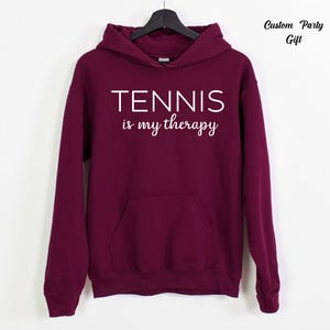A maroon hoodie with the text "TENNIS is my therapy" printed on it.