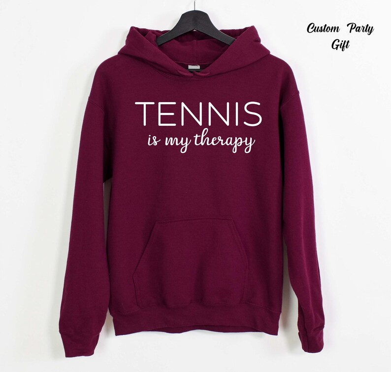 A maroon hoodie with the text "TENNIS is my therapy" printed on it.