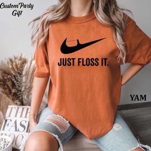 a woman wearing an orange shirt that says just floss it