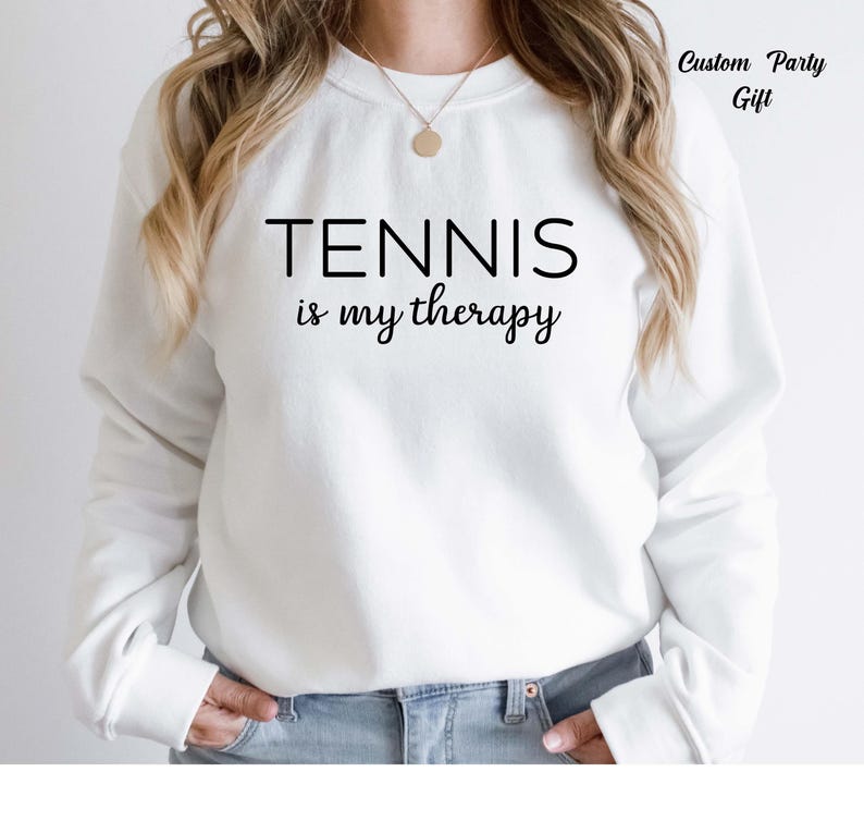 A person wearing a white sweatshirt with the text "TENNIS is my therapy" printed on it.