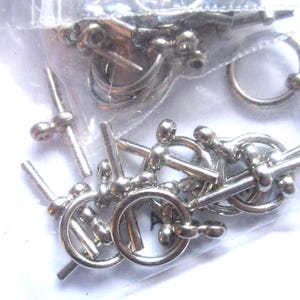 May include: A close-up of silver-toned metal clasps with a round ring and a straight bar. The clasps are in a clear plastic bag.