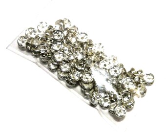 May include: A clear plastic bag filled with numerous silver-colored, rhinestone-studded beads. Each bead has a circular, flower-like design with a central rhinestone and surrounding smaller rhinestones. The beads are likely for jewelry making or craft projects.