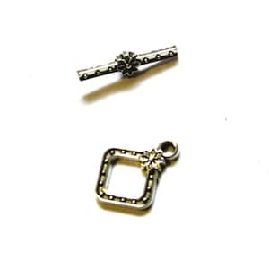 May include: Two silver-toned jewelry clasps. One is a rectangular bar with a floral accent in the center. The other is a square with a floral accent and a loop. Both clasps have small dot details.