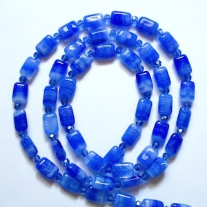 May include: A necklace composed of cylindrical blue and white swirled glass beads interspersed with small, faceted translucent blue crystal beads. The beads are arranged in a continuous circular pattern, showcasing a repeating color gradient.