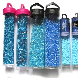 May include: Assortment of seven small tubes filled with various shades of blue glass seed beads. The tubes have black and pink lids with a carrying handle.