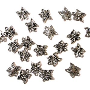 May include: Scattered across a white surface are numerous small, silver-colored butterfly charms. Each charm features a detailed, openwork design with four wings and a small loop for attachment, ideal for jewelry making or crafting.