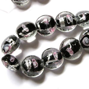 May include: A strand of round glass beads with black and silver accents and pink swirls. The beads are translucent and have a glossy finish.