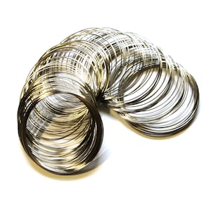 May include: A collection of silver-colored metal rings, tightly coiled together, arranged in a curved shape against a white background. The rings appear to be made of thin wire, reflecting light and creating a shiny appearance. The overall effect is of a decorative or craft element.