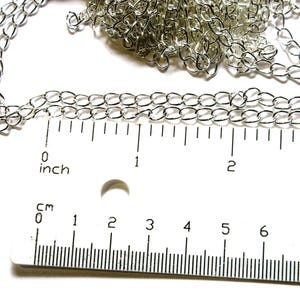 May include: Close-up of a silver-colored chain with oval links. A ruler with inch measurements is placed next to the chain. The chain is approximately 2 inches long.