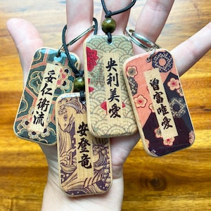 May include: Four wooden rectangular pendants with Japanese text and decorative patterns. Each pendant is attached to a black cord with a wooden bead. The pendants feature various colors, including green, red, and brown.