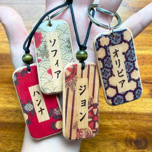 Peut inclure: Quatre porte-clés rectangulaires en bois avec des textes japonais et des motifs décoratifs. Chaque porte-clés présente un design différent, avec des fonds floraux rouges, rayés et à motifs. Les porte-clés sont attachés à des cordons noirs avec des perles en bois et des anneaux porte-clés en métal.