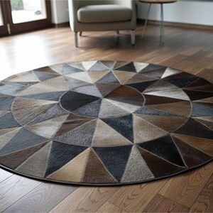 May include: A round rug with a geometric pattern in shades of brown, gray, and black. The rug is made of a material that appears to be hide or leather, with a dark border. The rug is placed on a hardwood floor.