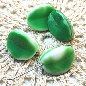 May include: Four smooth, rounded glass beads featuring a marbled pattern of vibrant green and opaque white. One bead is threaded onto a thin silver-toned metal headpin, while the other three beads are arranged in a cluster around it.