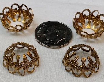 May include: Four gold-colored metal bead caps with a decorative design. The caps are about the size of a US dime.