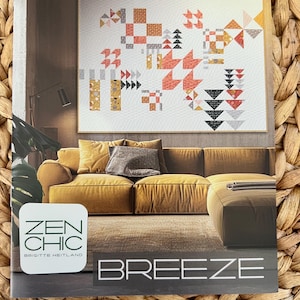 May include: A magazine cover featuring a quilt with geometric patterns in shades of orange, gray, and black. The quilt hangs above a mustard-colored sofa with decorative pillows. The text "ZEN CHIC" and "BREEZE" are visible.