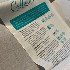 May include: A close-up of a white and teal Callie Del Interfacing product description. The text describes the product's use for quilting, bag making, and garment construction. The product is designed to add body and stability to fabrics.