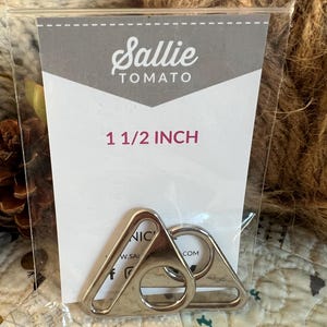 May include: Two silver 1 1/2 inch D-rings in a clear plastic bag with a white card that says "Sallie Tomato" and "1 1/2 inch".