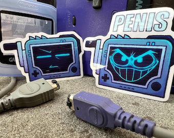 May include: Two blue and white Game Boy Advance game cartridge stickers. One sticker features a pixelated face with a menacing expression and the word "PENIS" above it. The other sticker features a pixelated face with a neutral expression.