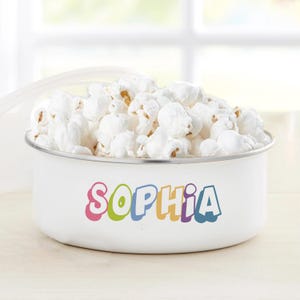 May include: White enamel popcorn bowl with a colorful "Sophia" name on the front. The bowl is filled with popcorn.