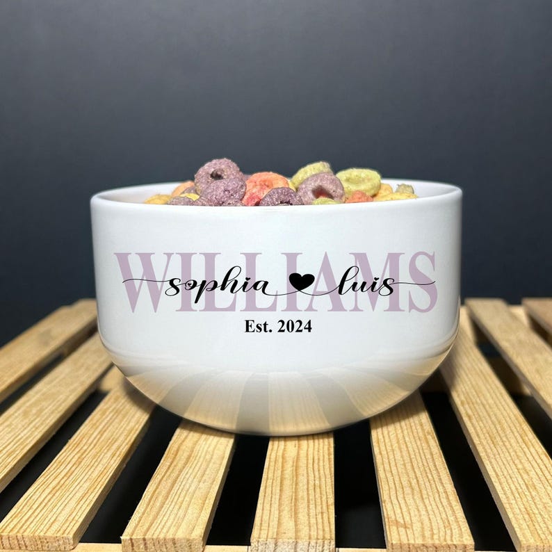 May include: A white ceramic bowl filled with colorful cereal loops. The front features the text "WILLIAMS" in large light purple letters, with "sophia" and "luis" in black script separated by a heart, and "Est. 2024" printed below in black.