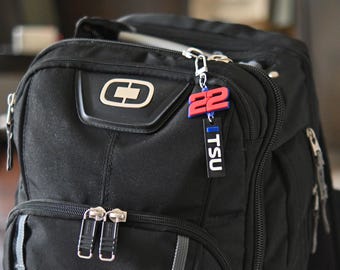 May include: Black backpack with silver zippers and a keychain. The keychain has the number "22" in red and blue, and a black tag that says "TSU" in white.