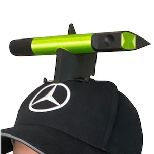 May include: A black baseball cap with a white logo, featuring a neon green and black device attached to the top. The device has a cylindrical shape with a pointed end.
