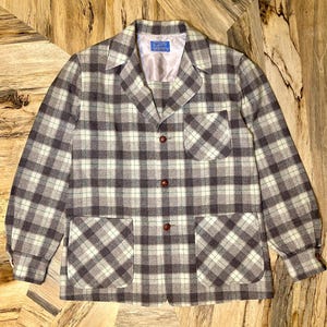 Puede incluir: Chaqueta vintage a cuadros en tonos grises, blancos y marrones. La chaqueta presenta un cuello cl&aacute;sico, dos bolsillos delanteros y botones marrones. La tela tiene una textura tejida.