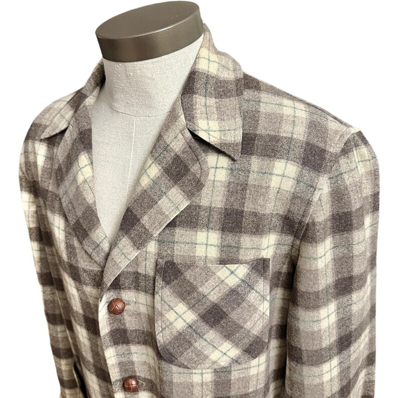 Puede incluir: Chaqueta a cuadros en tonos marr&oacute;n, crema y verde, exhibida en un maniqu&iacute;. La chaqueta presenta un cuello con solapas, un bolsillo en el pecho y dos botones marrones. La tela tiene un aspecto cl&aacute;sico y vintage.