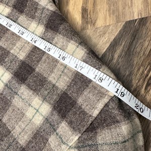 Puede incluir: Primer plano de una tela a cuadros marr&oacute;n y beige con una cinta m&eacute;trica blanca. La cinta muestra medidas de 30 a 51 cm. La tela tiene una paleta de colores cl&aacute;sica y neutra.