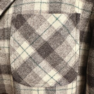 Puede incluir: Primer plano de una chaqueta a cuadros gris, marr&oacute;n y crema con un bolsillo. La chaqueta tiene un patr&oacute;n de cuadros cl&aacute;sico con una mezcla de colores y texturas. El bolsillo es de un tono marr&oacute;n m&aacute;s oscuro y la costura es visible.