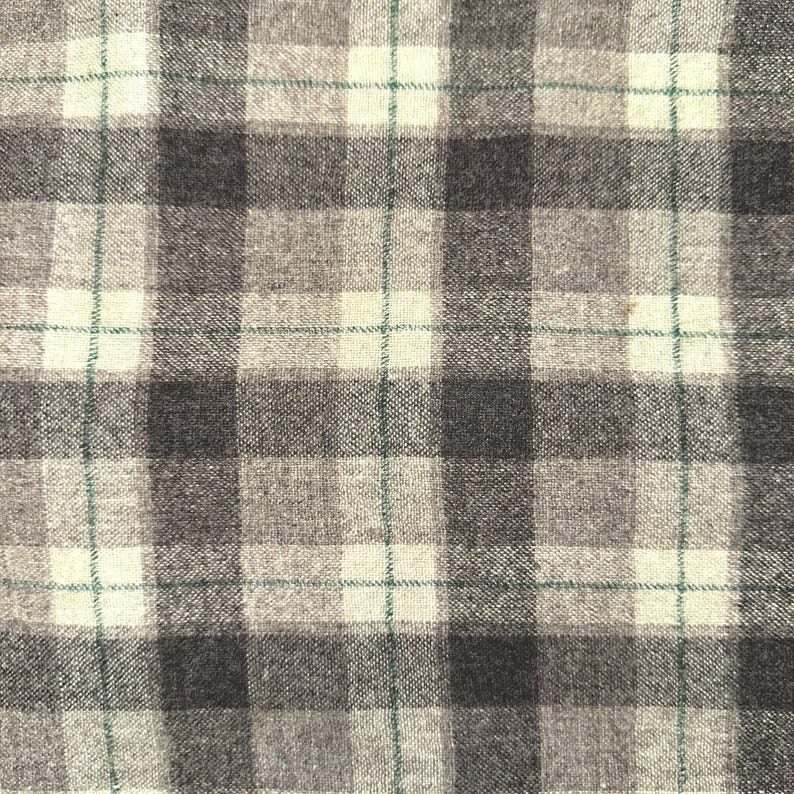 Puede incluir: Primer plano de una tela con un patr&oacute;n de cuadros. El dise&ntilde;o presenta una cuadr&iacute;cula de cuadrados grises oscuros, grises claros y blanquecinos alternados. Finas l&iacute;neas verdes intersectan el patr&oacute;n. La tela tiene una apariencia texturizada.