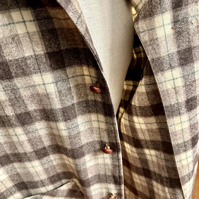 Puede incluir: Primer plano de una camisa abotonada a cuadros marr&oacute;n, beige y verde. La camisa tiene botones marrones y un forro beige. El estampado de cuadros es un dise&ntilde;o cl&aacute;sico, adecuado para ropa informal.