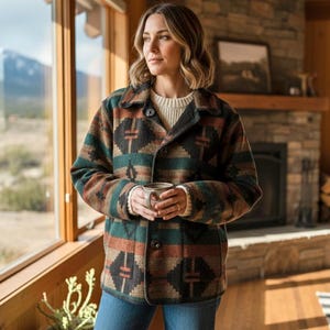 May include: A button-down jacket with a geometric pattern in shades of green, brown, and black. The jacket has a collared neckline and is worn over a cream-colored sweater. The jacket is made of a thick, textured fabric.