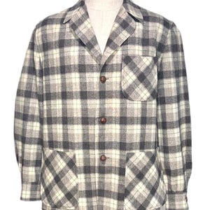 Puede incluir: Chaqueta a cuadros grises, blancos y negros con tres botones marrones y dos bolsillos delanteros. La chaqueta se exhibe en un maniqu&iacute; y tiene cuello y mangas largas. La tela parece ser una mezcla de lana.