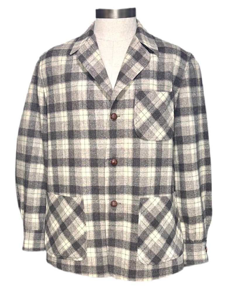 Puede incluir: Chaqueta a cuadros grises, blancos y negros con tres botones marrones y dos bolsillos delanteros. La chaqueta se exhibe en un maniqu&iacute; y tiene cuello y mangas largas. La tela parece ser una mezcla de lana.