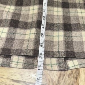 Puede incluir: Primer plano de una tela a cuadros en tonos marr&oacute;n, beige y verde. Una cinta m&eacute;trica se coloca verticalmente a lo largo de la tela, mostrando medidas de 61 a 81 cm.