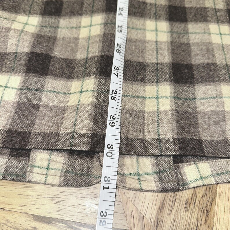 Puede incluir: Primer plano de una tela a cuadros en tonos marr&oacute;n, beige y verde. Una cinta m&eacute;trica se coloca verticalmente a lo largo de la tela, mostrando medidas de 61 a 81 cm.