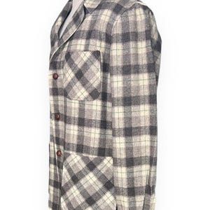 Puede incluir: Chaqueta a cuadros gris y crema con dos bolsillos delanteros y botones marrones. La chaqueta se exhibe en un maniqu&iacute; y tiene un dise&ntilde;o cl&aacute;sico y a medida. El patr&oacute;n de cuadros es una mezcla de gris, crema y un toque de verde.