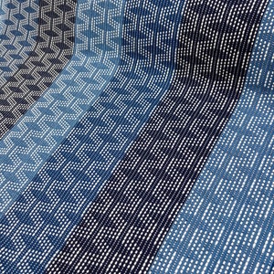 May include: A close-up of a blue and white patterned fabric with a woven texture. The fabric is made up of vertical stripes with different patterns, including small white dots, diagonal lines, and geometric shapes.