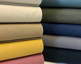 May include: A stack of fabric rolls in various colors, including white, beige, yellow, pink, blue, green, and gray. The fabric is a soft, textured material.