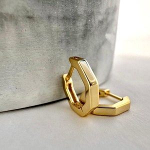 May include: A pair of gold hexagonal hoop earrings. The earrings are simple and modern in design.